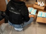 fotografia przedstawia funkcjonariusza Służby Celno-Skarbowej na tle otwartego opakowania kartonowego zawierającego leki.