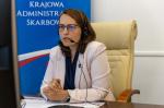Fotografia przedstawia siedzącą za biurkiem szefową KAS Magdalenę Rzeczkowską