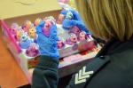 Funkcjonariuszka Służby Celno-Skarbowej w gumowych rękawiczkach wyjmuje z opakowania zbiorczego zabawki w jaskrawych kolorach i z bliska je ogląda 