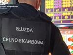 Funkcjonariusz w kamizelce z napisem Służba Celno-Skarbowa, w tle zarekwirowane automaty