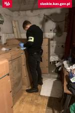 funkcjonariusz przeszukuje garaż wypełniony paczkami z suszem tytoniowym