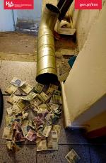 Gotówka porozrzucana na podłodze, obok rura i schody.