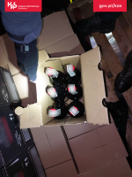 Funkcjonariusz otwiera karton, w którym znajduje się sześć butelek z alkoholem.