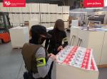 funkcjonariusze Służby Celno-Skarbowej stojący obok wydrukowanych arkuszy z logiem podrabianej marki papierosów