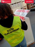 funkcjonariusz Służby Celno-Skarbowej trzymający wydrukowany arkusz z logiem podrabianej marki papierosów