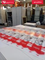 fragment linii technologicznej produkującej opakowania do papierosów, na pierwszym planie palety z wydrukowanymi arkuszami z logiem podrabianej marki papierosów