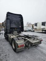 Widok na tył ciemnego ciągnika siodłowego, który stoi przy budynku przemysłowym.