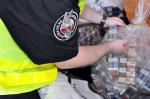 Funkcjonariusz Krajowej Administracji Skarbowej otwiera worek zawierający paczki z papierosami nielegalnego pochodzenia.