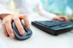 Zdjęcie przedstawia mysz komputerową wraz z klawiaturą do komputera oraz dłonie osoby, które je obsługują.